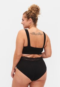 Zwarte soft-cup bralette met brede bandjes en een gladde afwerking, gecombineerd met hooggesneden zwarte onderbroek met kant langs de tailleband.