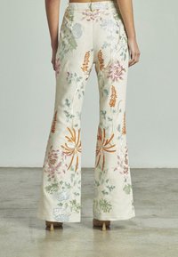 Pantaloni svasati ricamati di colore avorio con motivi floreali colorati. Presentano un design a gamba larga e una leggera lucentezza nel tessuto.