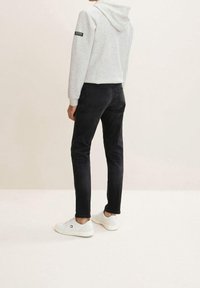 Grå hoodie med dragsko i huvan, svarta slim fit jeans och vita sneakers. Notabel etikett på vänster ärm. Släta texturer överallt.