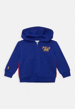 Felpa con zip per bambini di colore blu, con cappuccio, tasche frontali, strisce laterali rosse, testo giallo "POLO 1967 ATHL. DEPT." e piccolo logo di cavallo sulla manica sinistra.