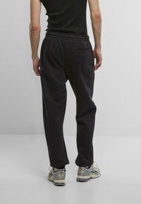 Black sweatpants with an elastic waistband, side pockets, and a rear pocket. Worn with light grey and silver athletic shoes.