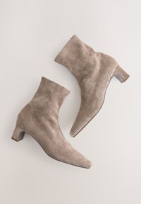 Beige suede ankle boots with a pointed toe and block heel. Features a sleek silhouette and visible stitching details.