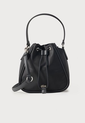 Bolso tipo cubo negro con asa superior y correa de hombro ajustable, cierre con cordón y pequeño logotipo plateado de cocodrilo en el centro delantero.