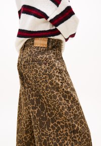 Jeans w leopardzim nadrukiem w odcieniach brązu i czerni, z skórzaną metką z napisem "TOMMY JEANS" na pasku oraz klasycznym pięciopocketowym wzornictwem.