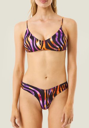 Donna che indossa un bikini a due pezzi con motivo astratto a strisce nere, arancioni e viola su sfondo uniforme.