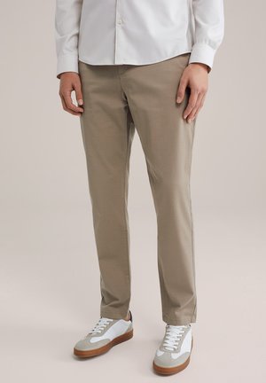 Lichtbeige chino's met een gladde textuur, slim fit en zijzakken, gecombineerd met witte sneakers met grijze en bruine accenten.