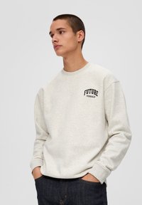 Helle graue Sweatshirt mit geripptem Kragen und Bündchen. Auf der Vorderseite steht der Text "FUTURE VISUALS" in Schwarz. Trägt es mit dunkler Jeans.