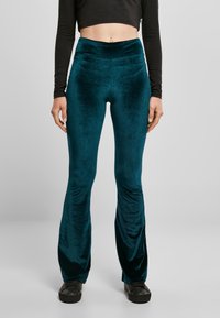 Spodnie z aksamitu w kolorze morskim o szerokich nogawkach i gładkiej fakturze, z wysokim stanem. Charakteryzują się delikatnym połyskiem i są zestawione z kontrastującym, czarnym, krótko skrojonym topem z długim rękawem.