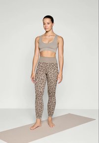 Beige sports-bh og tights med et brunt leopardmønster. Stoffet ser elastisk og glatt ut, egnet for atletiske aktiviteter.