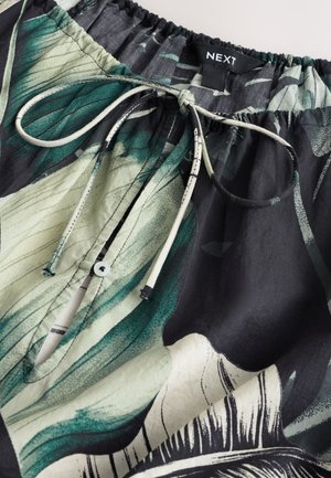 Nahaufnahme eines elastischen Bunds mit floralem grünen, schwarzen und weißen Stoff, mit gebundenem Kordelzug und geknöpftem Schlüsselloch-Öffnung.