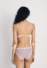 Ljust rosa lingerisett med en enkel bh med justerbara band och matchande mönstrade trosor med spetsdetaljer, sedd bakifrån.