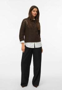 Pull en maille marron avec des sequins aux épaules, porté sur une chemise blanche. Assorti avec un pantalon large taille haute noir.