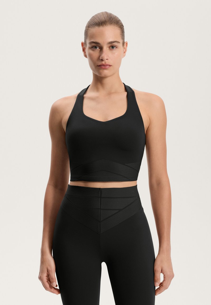 Čierny športový top s dizajnom do V, textúrovaným pásom a širokými ramienkami, skombinovaný s čiernymi legínami s vysokým pásom a textúrou, ktoré majú vzor chevron.