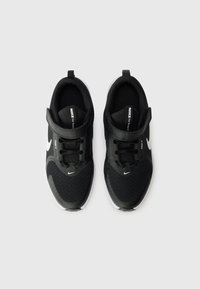 Schwarze Sportschuhe aus Mesh-Material, kontrastierendes weißes Nike-Logo, verstärkter Zehenbereich, verstellbarer Klettverschluss und strukturiierte Sohle.
