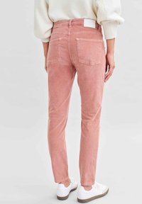 Roze corduroy broek met een slim fit, voorzien van achterzakken, een wit label op de tailleband en een gestructureerde oppervlakte. Gecombineerd met witte sneakers.