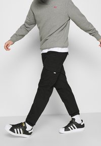 Šedá mikina, černé cargo kalhoty a černé tenisky Adidas s bílými detaily. Cargo kalhoty mají kapsy; mikina má malé červené logo.