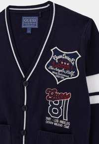 Cardigan blu navy con accenti a strisce bianche, dotato di toppe ricamate, bottoni e tasche. Realizzato in morbido tessuto a maglia.