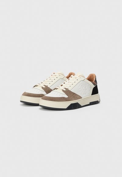 Låga sneakers med paneler i beige, brunt och svart, texturerat vitt läder på sidan, präglad logotyp och snörning på en vit bakgrund.