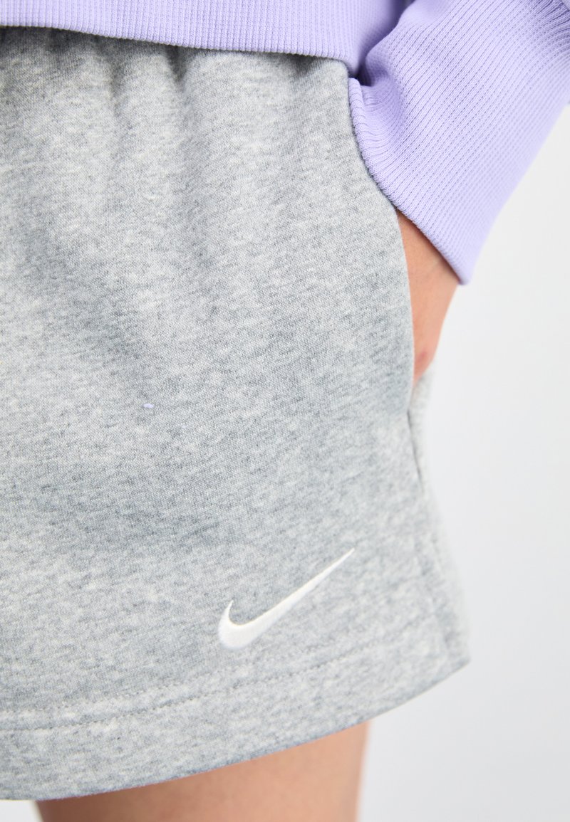 Szare, miękkie szorty z tkaniny z elastycznym paskiem w talii i kieszeniami; posiadają biały logo Nike w kształcie „swoosh” na dolnym końcu; zestawione z lawendową bluzką.