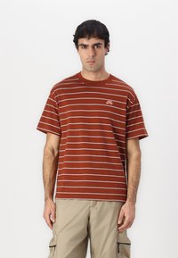 Brun stribet t-shirt med hvide vandrette linjer og et lille Nike-logo på brystet. Fremstillet af letvægts bomuldsstof.