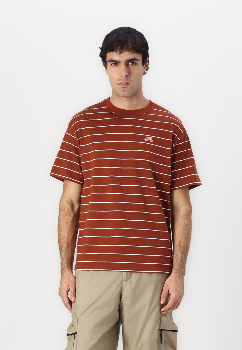 Brun stribet t-shirt med hvide vandrette linjer og et lille Nike-logo på brystet. Fremstillet af letvægts bomuldsstof.