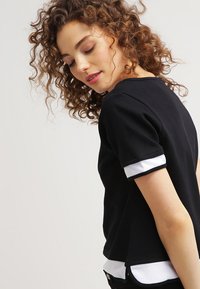 Top corto nero a maniche corte realizzato in cotone con accenti in rete bianca ai polsini e all'orlo. Presenta una vestibilità rilassata e un collo curvo.