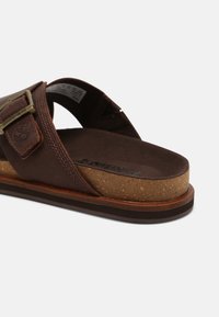 Sandale en cuir marron avec une semelle intermédiaire en liège, une sangle ajustable, des coutures détaillées et une semelle extérieure en caoutchouc. Présente le logo Timberland sur la sangle.