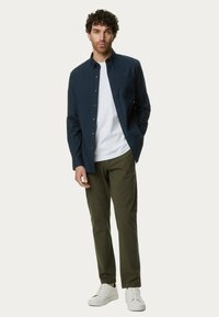 Camisa de botones navy sobre una camiseta blanca, combinada con pantalones verde oliva y zapatillas de deporte blancas; diseño casual y ajustado; tejido texturizado.