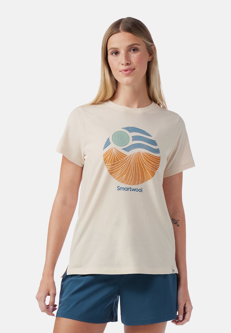 T-shirt couleur crème en mélange de coton avec un motif circulaire représentant un soleil stylisé et des montagnes en orange et bleu ; logo en dessous.
