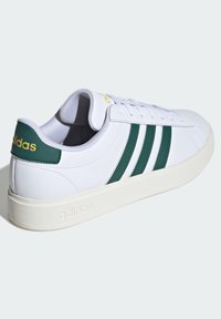 Biele tenisky so zelenými pruhmi, vyrobené z hladkého syntetického materiálu. Mäkký, polstrovaný jazyk a golier; žlté logo na päte.