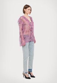 Caurspīdīga, violeta ziedu blūze ar volānu malām, kombinēta ar gaiši zilām taisnām džinsu biksēm un melniem slingbakveida papēžiem.