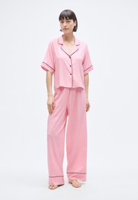 Σετ ροζ πιτζάμας με κοντομάνικο τοπ με κουμπιά και φαρδιά παντελόνια, διακοσμημένο με λευκές βούλες και μαύρο περιθώριο στις άκρες.