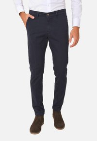 Chino in cotone blu navy con vestibilità aderente, dotati di tasche anteriori, chiusura con bottone e una consistenza morbida. Abbinati a scarpe in suede marrone.