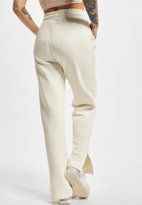 Cremefarvede sweatpants med en afslappet pasform, elastisk talje, sidelommer og slids ved kanten, lavet af blødt stof.