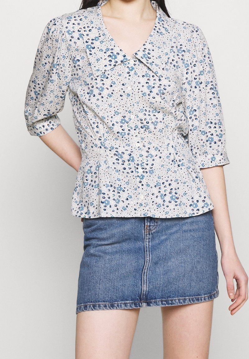 Blouse à motif floral en tissu léger avec un décolleté en V et des manches bouffantes, associée à une mini-jupe en denim. Les deux présentent une coupe décontractée.