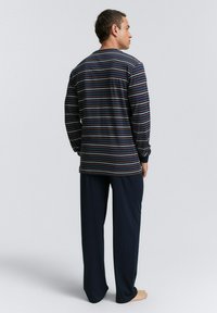 T-shirt à manches longues rayé en bleu marine, présentant des rayures multicolores. Associé à un pantalon ample bleu marine, offrant une coupe décontractée et une texture douce.
