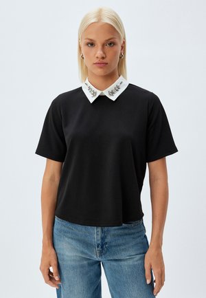 Zwart kortmouwtop met een witte kraag versierd met decoratieve elementen. Gladde stof, losse pasvorm en een ronde zoom.
