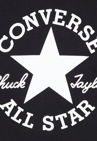 Tissu noir présentant une grande étoile blanche avec "Converse" et "Chuck Taylor All Star" imprimés en polices grasses et en script autour.