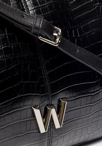 Bolso de mano de cuero sintético negro con una correa negra y un brillante emblema dorado con la letra "W" en la parte frontal.
