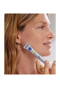 Nivea Q10 gezielt gegen feine Linien Filler in einer silbernen Tube, nah an der Wange gehalten, mit aufgetragenen Cremepunkten auf der Haut für die Hautpflegeanwendung.