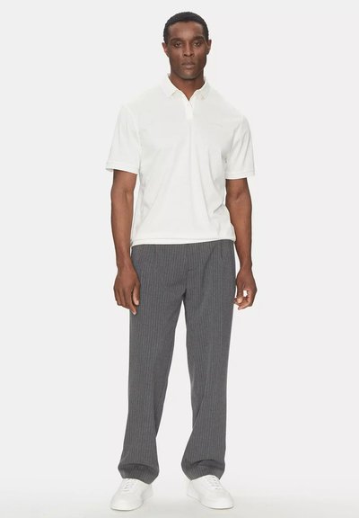 Polo bianco con maniche corte e colletto, abbinato a pantaloni grigi a righe sottili e sneakers bianche. Design semplice e lineare.