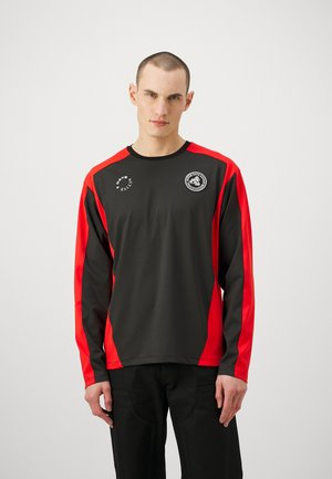 Long-sleeve athletic shirt, black with red side accents, made from smooth synthetic material, featuring logos on the chest and sleeves.
