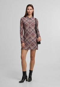 Rochie cu guler, în carouri, de culoare mov cu accente albastre. Mâneci lungi și tiv ondulat. Purtați cu cizme negre până la gleznă și o geantă mică neagră.