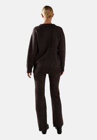 Maglione marrone scuro lavorato a maglia e pantaloni svasati coordinati, caratterizzati da un orlo a coste e una vestibilità comoda, mostrati di spalle con una trama liscia.