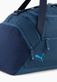 Sac de sport bleu marine avec une finition texturée, arborant un logo Puma turquoise, des poches à double zip et une bandoulière réglable.