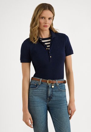 Mörkblå pikétröja med korta ärmar och knappkrage. Kombinerad med ljusblå jeans och ett brunt bälte med ett gyllene spänne. Randig skjorta under.