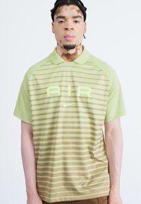 Polo vert et beige à rayures, fabriqué en tissu léger, avec un col, des manches courtes et un logo "AIR" en vert clair.