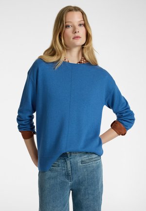 Blauwe trui met een ontspannen pasvorm, ronde halslijn en lange mouwen. Bruine accenten op de manchetten. Gecombineerd met lichtblauwe denim jeans.