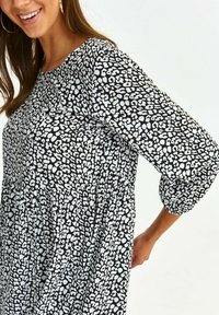 Svart och vit leopardmönstrad klänning med trekvartslånga ärmar, samlad midja och en flödande silhuett, som visar upp ett mjukt, texturerat tyg.