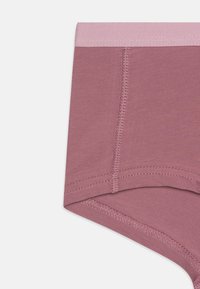 Sous-vêtements en coton rose court avec une ceinture élastique plate, présentant une texture lisse et des détails de couture visibles le long des bords.